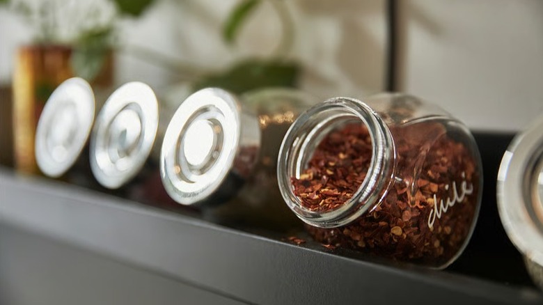 Row of RAJTAN spice jars, with one open and full of chili flakes