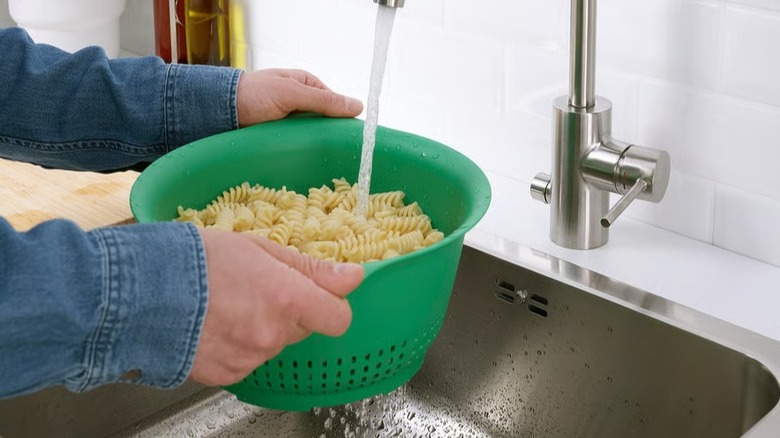 Person straining pasta in the green UPPFYLLD colander over a sink