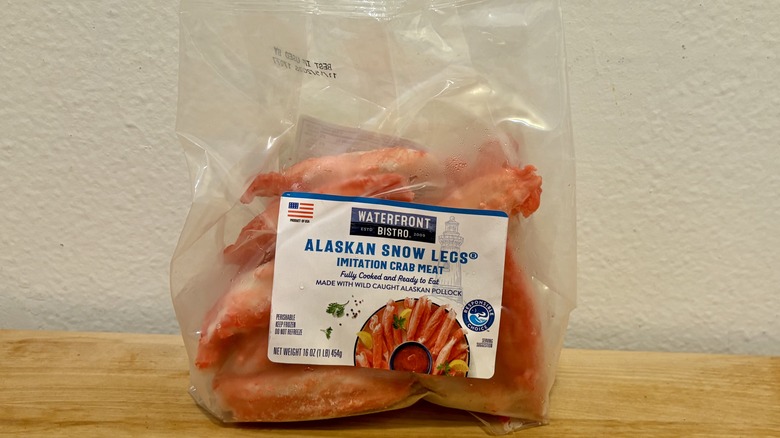 A bag of Waterfront Bistro Alaskan Snow Legs Imitation Crab Meat on a wooden table set against a whie wall