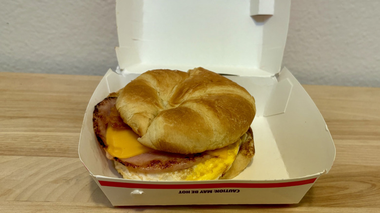A Supreme Croissant from Jack in the Box sitting on a wood table inside of its box