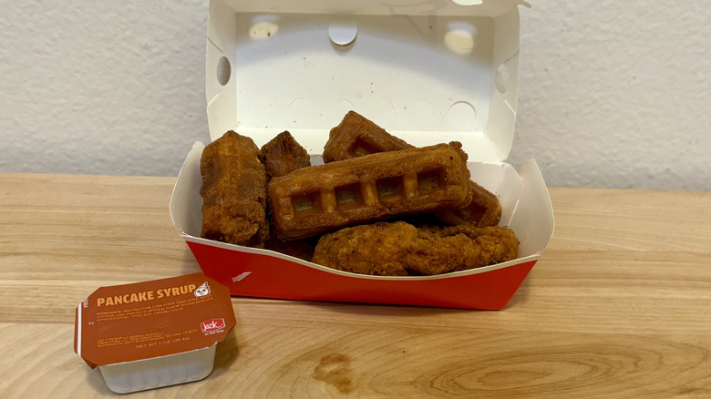 An order of Chicken and Waffles from Jack in the Box on a wood surface next to some pancake syrup