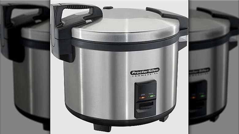 The Proctor Silex commercial rice cooker with the lid on and cook buttons lit up; the cooker is made of stainless steel.