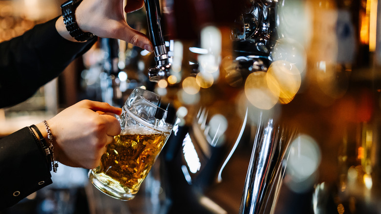 Bartender's hands pouring draft beer into a glass from the tap