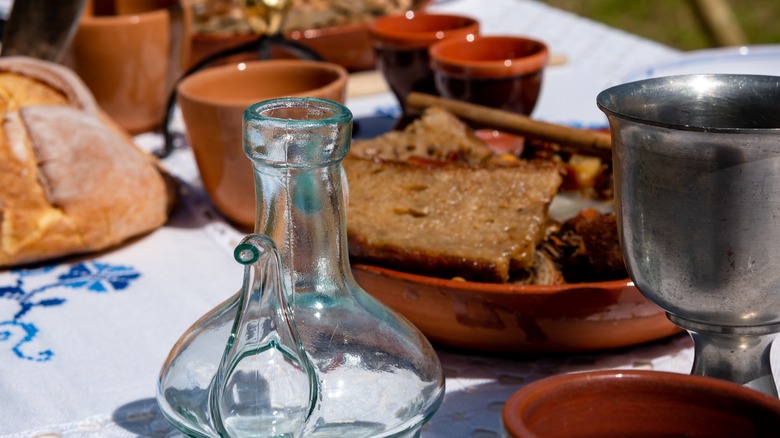 Table at a historical reenactment showing medieval dinnerware and a trencher soaked with the remains of a meal, in a plate