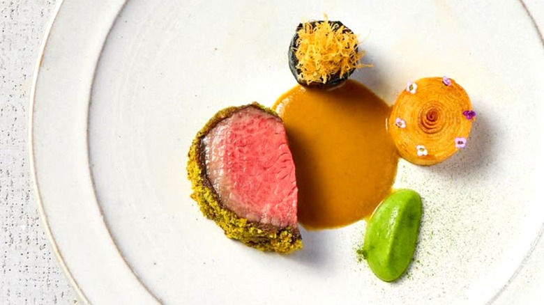 Beef entrée with assorted colorful side dishes and a brown sauce on a white plate