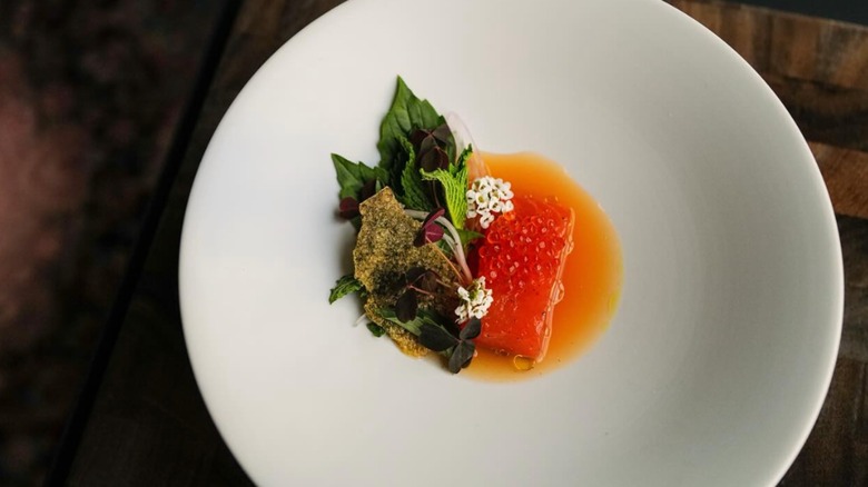 Poached fish with greens and edible flowers in a vibrant orange sauce on a white plate