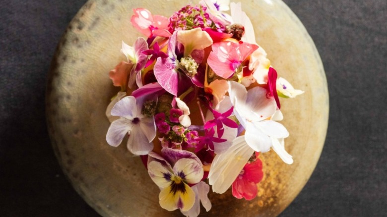 Dish composed of colorful edible flowers on a white foam served on a black plate