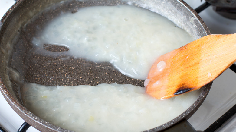 Person cooking roux in pan with a wooden spoon
