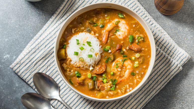 Bowl of Cajun gumbo on a striped towel with two spoons resting nearby