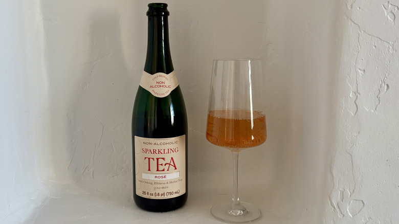 A glass of Non-Alcoholic Rosé Sparkling Tea next to its bottle.
