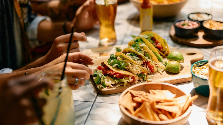 A plate of tacos with tortillas chips and salsas on a table