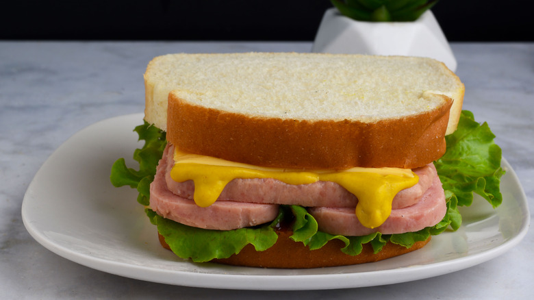 A spam, lettuce, and yellow mustard sandwich on white bread on a plate
