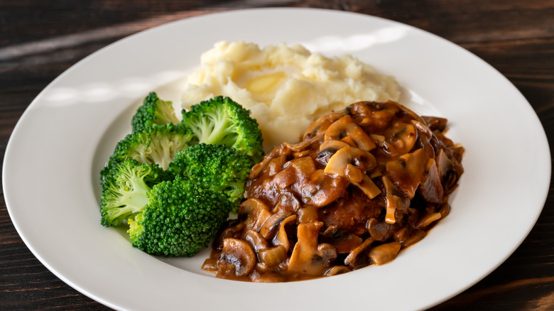 A plate of Salisbury Steak with steamed broccoli and mashed potatoes