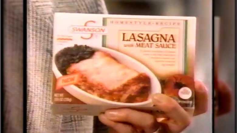A man's hand holding a box of Swanson Homestyle Entree Lasagna with Meat Sauce