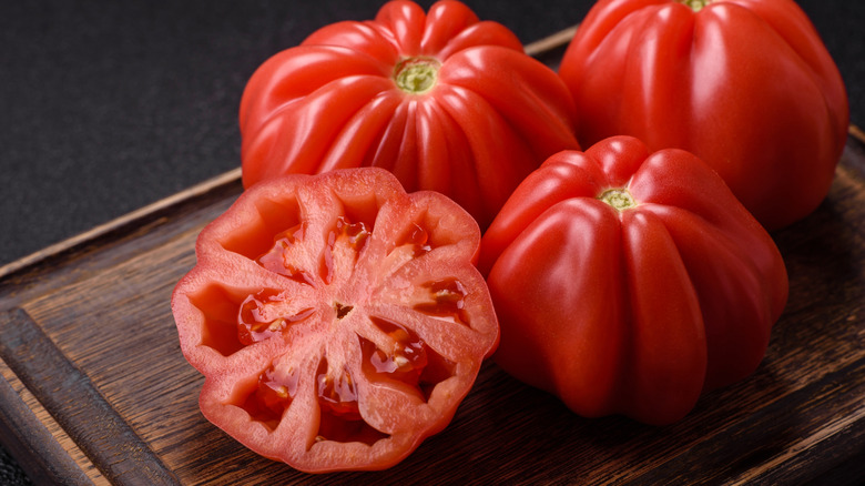 Fresh heirloom tomatoes sitting on a wooden cutting board, one is cut in half