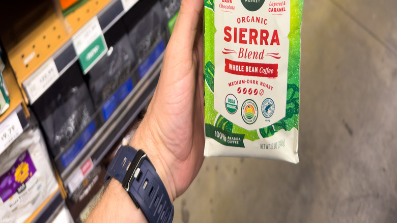 A person holding a bag of Whole Foods coffee in front of the coffee shelf