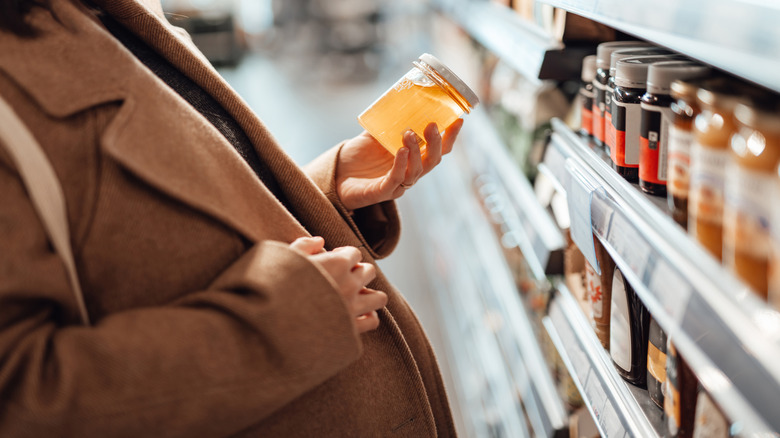 woman looking at a jar of honey from the supermarket shelf