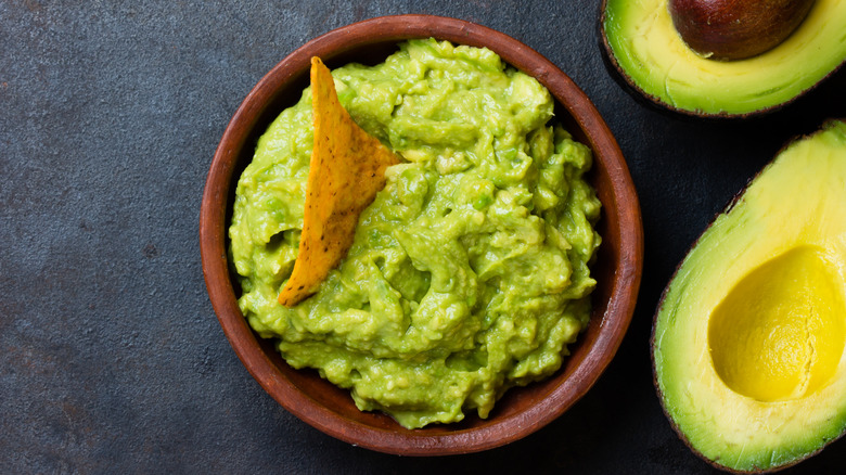 Bowl of guacamole next to avocado halves