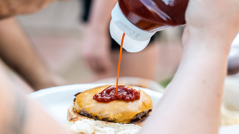 Person squirting ketchup on burger