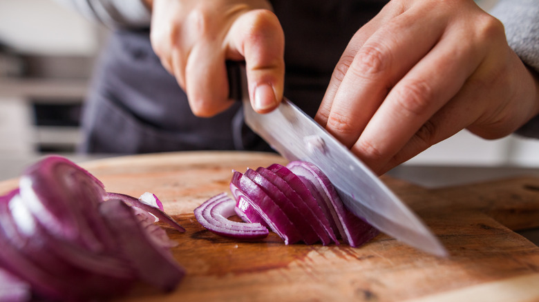 Person slicing red onions on cutting board