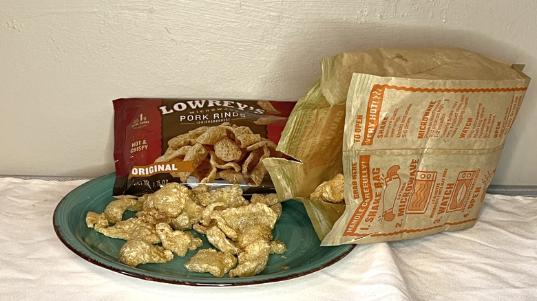 An opened bag of Lowrey's pork rinds spilling out onto green plate