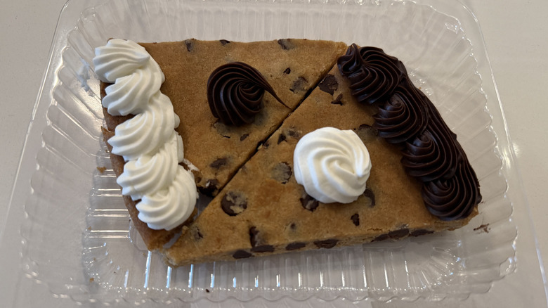 Two cookie cake slices with vanilla and chocolate icing in a plastic container on a white table