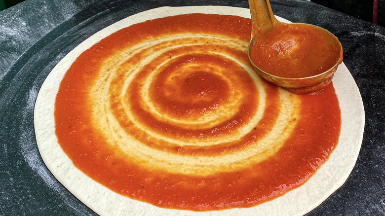 Sauce being ladled and spread on pizza dough
