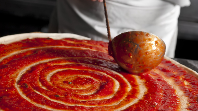ladle spreading sauce on pizza