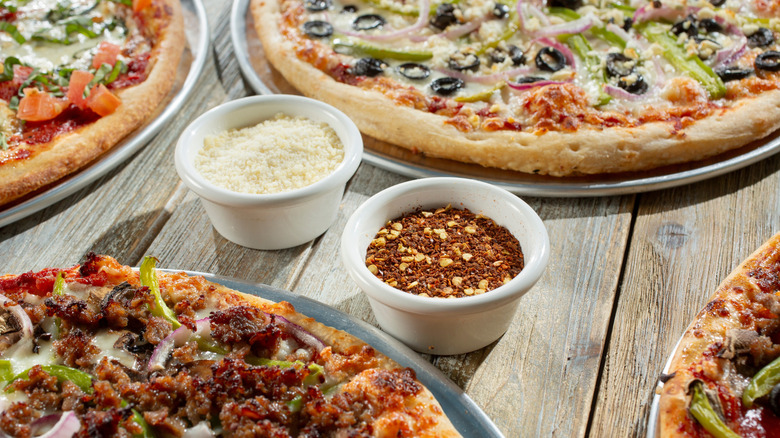 Side containers of red pepper flakes and grated parmesan next to pizzas