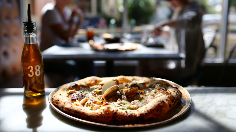 clam wood-fired pizza sitting on the counter at a restaurant, next to a bottle of olive oil