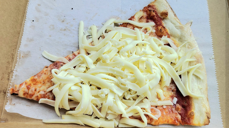 cold mozzarella on top of a cheese pizza slice in a box