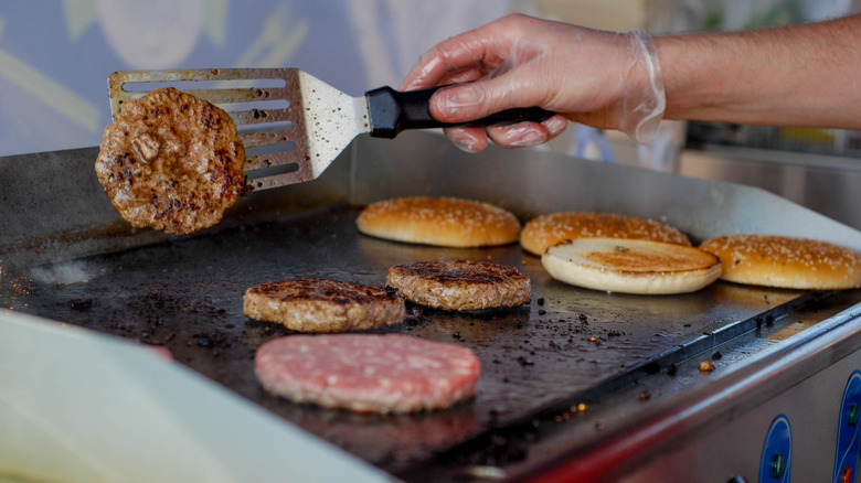 Hand flipping burgers on a griddle