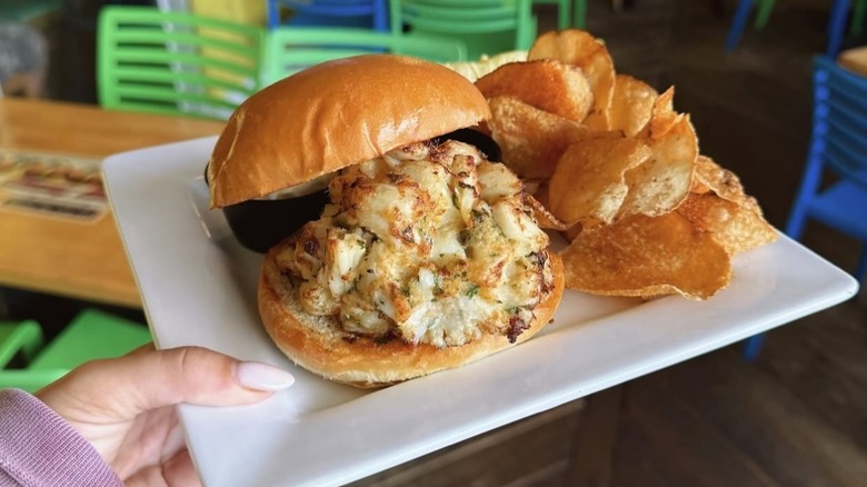 A person holding a plate with a crab cake sandwich and potato chips at Woody's Dewey Beach in Dewey Beach