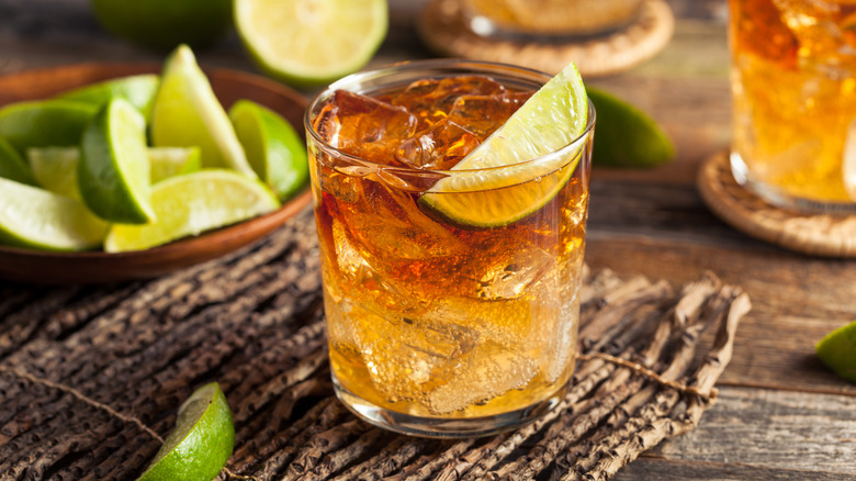 Rum drink in a glass with a lime wedge with a bowl of lime wedges and other drinks in the background