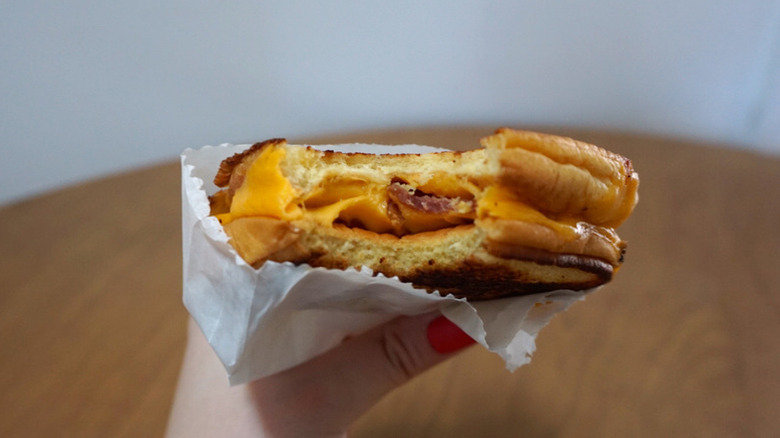 A hand holding a half-bitten Bacon Grilled Cheese Sandwich from Shake Shack