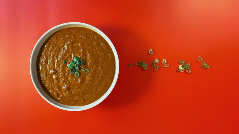 A bowl of chili on a red background with green onions
