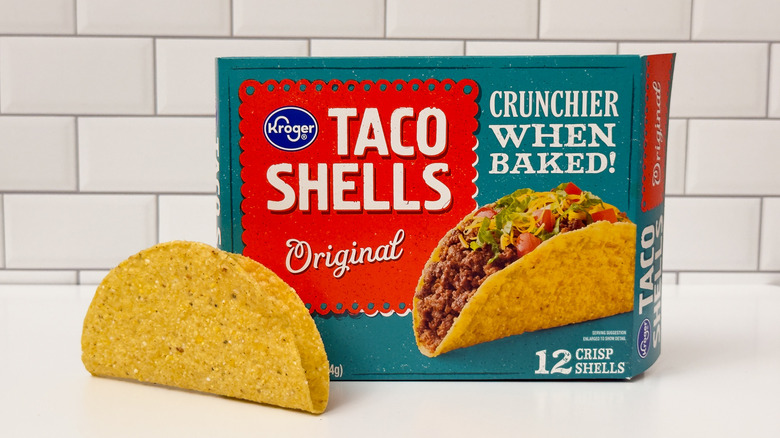 A box of Kroger brand hard taco shells, with a taco outside the box on the left side