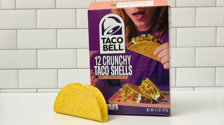 A box of Taco Bell crunchy taco shells, with a taco outside the box on the left side