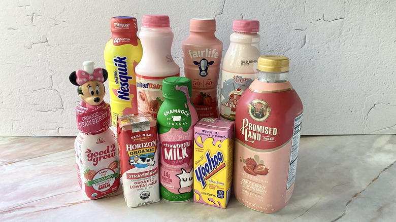 Rows of nine different brands of strawberry milk in their original bottles and cartons