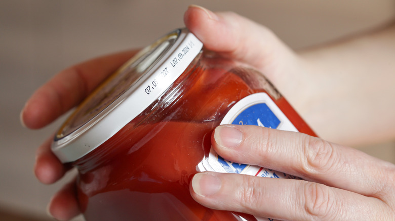 Someone holding a jar of tomatoes to examine expiration date on the lid