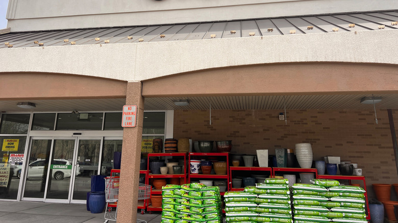 Under the eaves of an Ollie's store, stacks of soil and large garden pots are on display