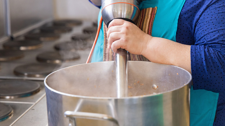 A chef uses an immersion blender in a pot
