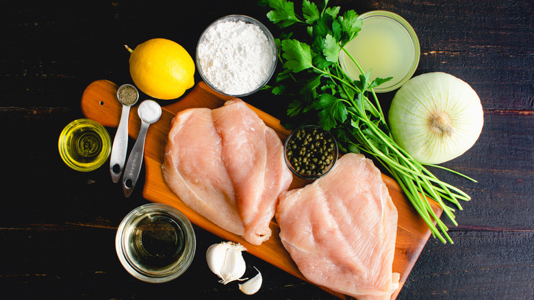 Chicken piccata mise en place with herbs, raw onions, fresh lemon, and capers