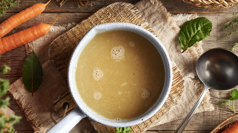 A large pot of vegetable stock on a wicker mat with a ladle next to it