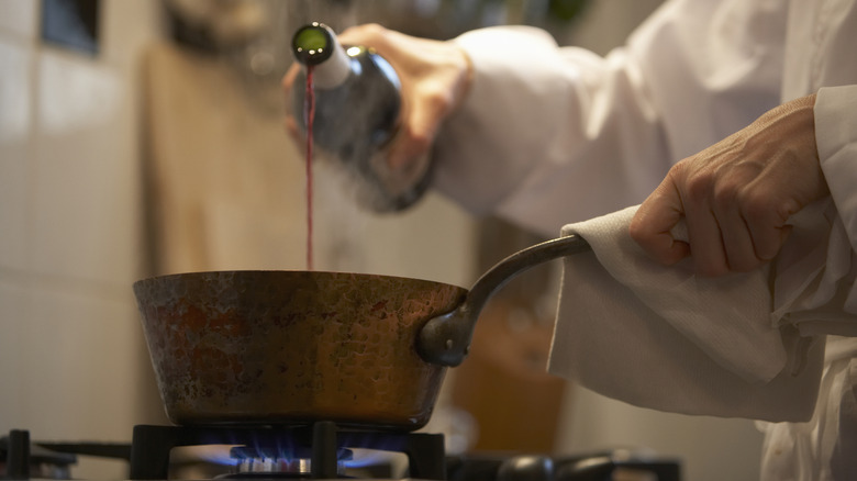 A chef pours wine into a pot
