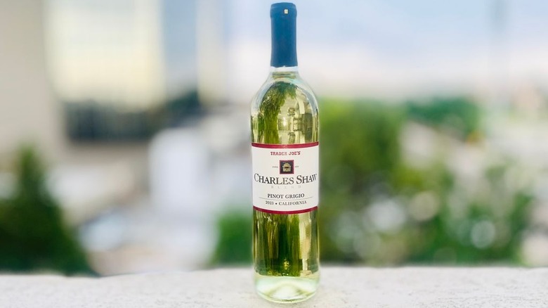 A bottle and a glass of Charles Shaw Pinot Grigio sitting on an outdoor ledge in sunlight