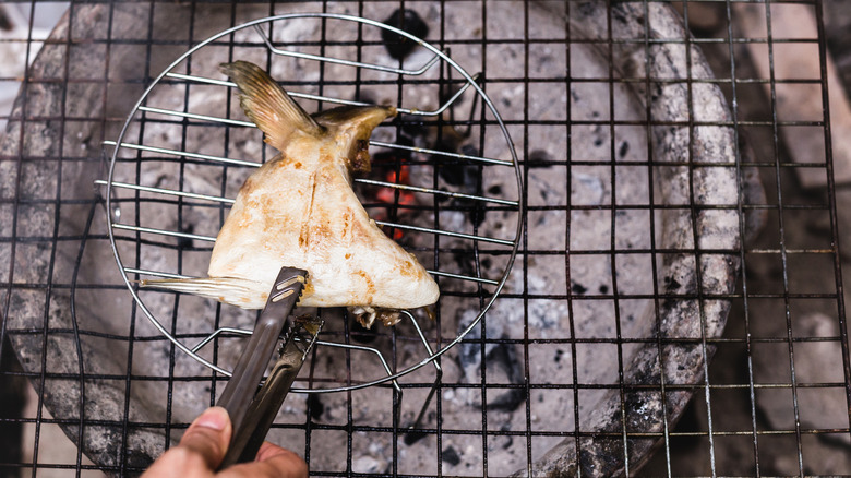 a man grilling a yellowtail fish cheek over a charcoal grill