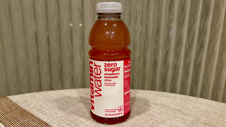 A Shine Zero Sugar Strawberry Lemonade Vitaminwater sitting on a table in front of a white curtain