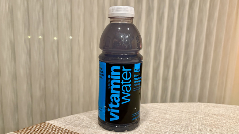 A Elevate Blue Raspberry Limeade Vitaminwater sitting on a table in front of a white curtain