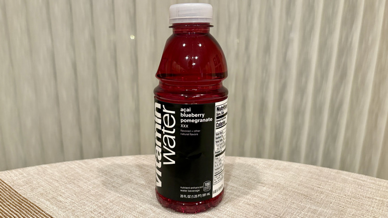 A XXX Acai Blueberry Pomegranate Vitaminwater sitting on a table in front of a white curtain